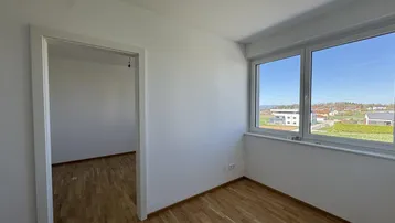 Geräumiges Zimmer mit Parkettboden und großen Fenstern, die einen weiten Blick auf die Landschaft bieten.