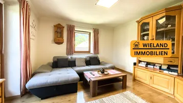 Gemütliches Wohnzimmer mit großem Ecksofa, Holzmöbeln und Blick ins Grüne.