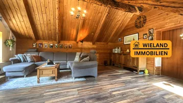 Gemütliches Wohnzimmer mit Holztäfelung, sichtbaren Balken und bequemer Sitzecke unter dem Dach.