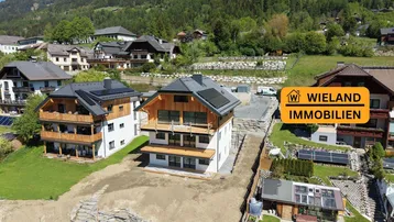 Luftaufnahme von zwei modernen Neubauten in alpiner Umgebung mit Bergblick und Baustelle.