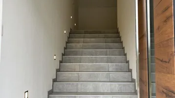 Heller Treppenaufgang mit modernen Fliesenstufen und integrierter Wandbeleuchtung.