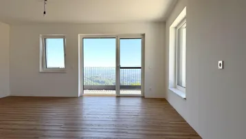 Helles Wohnzimmer mit Holzboden und Zugang zu einem Balkon mit weitreichendem Ausblick.