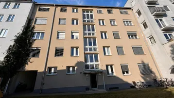 Fassade eines Mehrfamilienhauses mit mehreren Balkonen und Fenstern unter blauem Himmel.