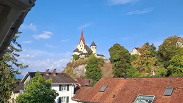 Malerischer Ausblick auf ein Dorf mit einer Kirche auf einem Hügel unter blauem Himmel.
