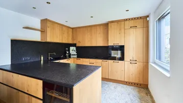 Moderne Küche mit Holzfronten, dunkler Arbeitsplatte, Kücheninsel und integrierten Geräten.