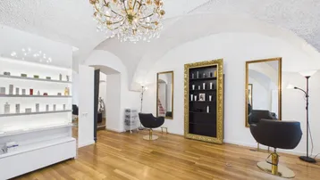 Heller Gewerberaum mit hohen Gewölbedecken, Holzboden und eleganten Friseurstühlen und Regalen.