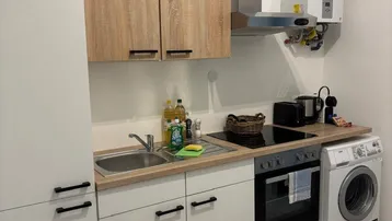 Kleine, funktionale Küche mit hellen Schränken, integriertem Backofen und Dunstabzugshaube.