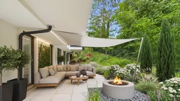 Großzügige Terrasse mit bequemen Loungemöbeln, Feuerstelle und üppiger Bepflanzung im Grünen.