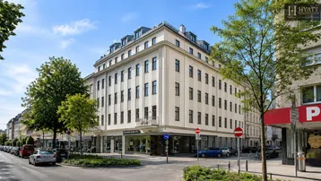 Großes Mehrfamilienhaus an einer Straßenecke mit klassischer Architektur und vielen Fenstern.