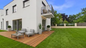 Moderne weiße Hausfassade mit großer Holzterrasse, Gartenmöbeln und gepflegtem Rasenbereich.