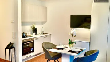 Moderne Küchenzeile mit Essbereich und integriertem Fernseher in hellem Ambiente.
