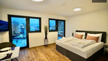 Helles Schlafzimmer mit großem Bett, Holzboden und Zugang zu einem Balkon oder einer Terrasse.