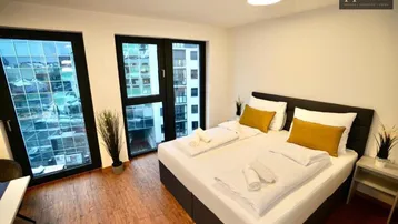 Helles Schlafzimmer mit Doppelbett, Holzboden und großen Fenstern mit Stadtblick.