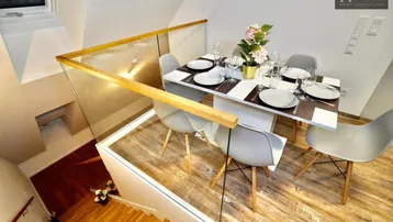 Moderner Essbereich mit Holzboden, gedecktem Tisch und Glasgeländer, unter einem Dachfenster gelegen.