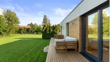 Moderne Holzterrasse mit bequemen Gartenmöbeln und weitläufigem Rasenbereich, ideal zum Entspannen im Freien.