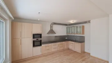 Helle Einbauküche mit Holzfronten, integriertem Backofen und Dunstabzugshaube in offenem Wohnbereich.