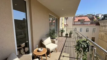 Geräumiger Balkon mit Holzboden, Sitzgelegenheiten und Blick auf die umliegenden Gebäude.