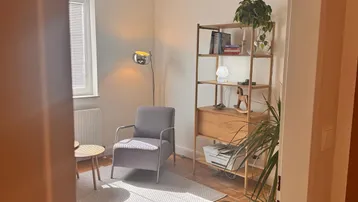 Einladendes Wohnzimmer mit Parkettboden, modernem Bücherregal und gemütlichem Sessel, durch einen Türrahmen fotografiert.