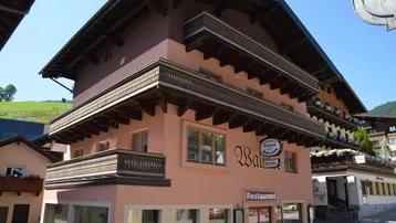 Traditionelles Gebäude mit rosa Fassade, Holzbalkonen und einem Restaurant im Erdgeschoss.