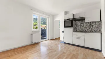 Heller Wohn-Essbereich mit integrierter Kochnische, Parkettboden und Zugang zum Balkon mit Bergblick.