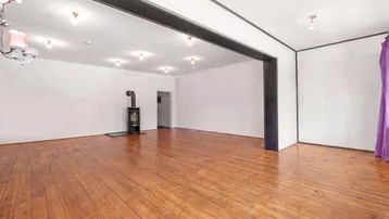 Geräumiger Wohnbereich mit glänzendem Holzdielenboden und einem gemütlichen Holzofen als Blickfang.