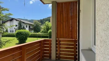 Heller Balkon mit Holzelementen, Fliesenboden und weitem Blick ins Grüne.