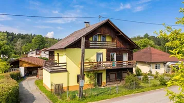 Freistehendes Haus mit gelber Fassade, Holzelementen und mehreren Balkonen in ländlicher Umgebung.
