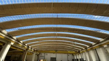 Große Industriehalle mit gewölbter Decke und viel Tageslicht durch zahlreiche Oberlichter, ideal für Lager oder Produktion.