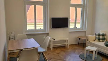 Heller Wohn- und Essbereich mit Fischgrätparkett, großen Fenstern und moderner Einrichtung.