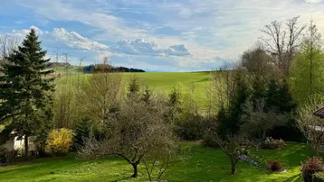 Weitläufiger Blick über grüne Felder und bewaldete Hügel unter einem blauen Himmel.