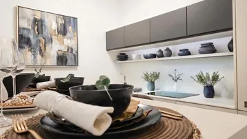 Moderne Küche mit dunklen Hängeschränken, beleuchteten Regalen und stilvoller Tischdekoration.