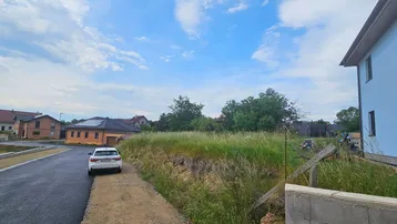 Blick auf ein unbebautes Grundstück mit angrenzender Straße und umliegenden Wohnhäusern unter blauem Himmel.