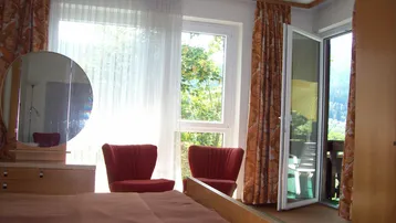 Schlafzimmer mit Doppelbett, Schminktisch und Zugang zu einem Balkon mit Bergblick.