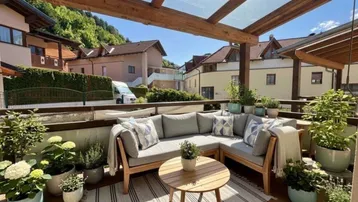 Sonniger Balkon mit gemütlicher Sitzecke, Holzpergola und Blick auf die grüne Umgebung.