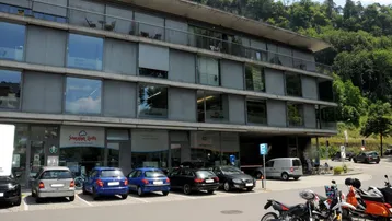 Modernes Geschäftsgebäude mit großen Glasfenstern und Balkonen, umgeben von Bäumen und Parkplätzen.