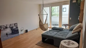 Helles Wohnzimmer mit Holzboden, gemütlichem Sofa und Zugang zum Balkon.