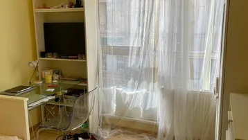 Helles Schlafzimmer mit Schreibtisch, Regal und großem Fenster, das viel Tageslicht hereinlässt.