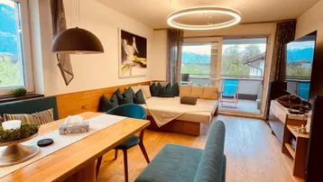 Heller Wohn- und Essbereich mit Holzboden, gemütlicher Sitzecke und Zugang zum Balkon.