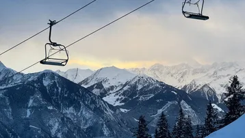 Winterliche Berglandschaft mit schneebedeckten Gipfeln und Skiliften unter einem bewölkten Himmel.