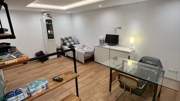 Helles Zimmer mit Laminatboden, integrierter Deckenbeleuchtung und einem Arbeitsbereich.