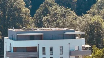 Modernes Apartmentgebäude mit mehreren Balkonen, umgeben von üppiger grüner Vegetation und Bäumen.