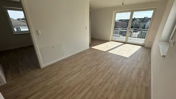 Heller Wohnbereich mit Parkettboden und Zugang zu einem Balkon, durchflutet von Tageslicht.