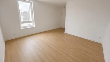 Helles, leeres Zimmer mit Laminatboden und weiß gestrichenen Wänden, bereit zum Einzug.