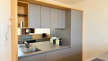 Moderne Küchenzeile mit grauen Schränken, integrierter Spüle und Kaffeemaschinen, minimalistisches Design.