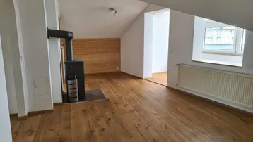 Geräumiges Wohnzimmer im Dachgeschoss mit Holzboden, Kaminofen und schrägen Wänden.