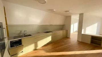 Helle, moderne Küche mit hellgrünen Einbauschränken, integrierten Geräten und Holzboden unter Dachschräge.