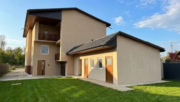 Modernes Haus mit beiger Fassade, dunklem Dach und großem, gepflegtem Rasenbereich.