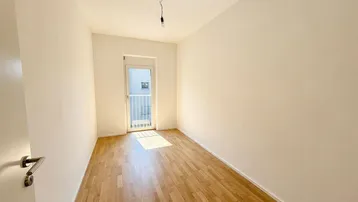Helles Schlafzimmer mit Holzboden und Zugang zu einem französischen Balkon.