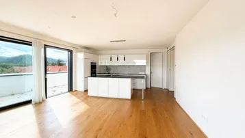 Heller offener Wohn- und Essbereich mit moderner Küche, Holzboden und Zugang zur Terrasse mit Bergblick.