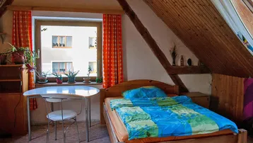 Gemütliches Schlafzimmer im Dachgeschoss mit Holztäfelung, Bett und einem kleinen Schreibtisch am Fenster.